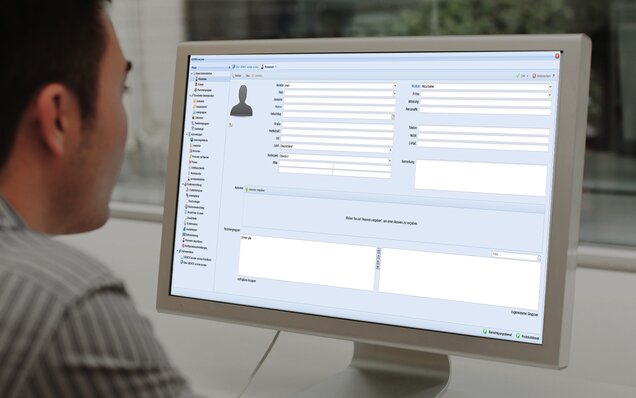 Eine Person sitzt vor einem Computerbildschirm. Auf dem Bildschirm ist die Software des Zutrittskontrollsystems GEMOS access zu sehen