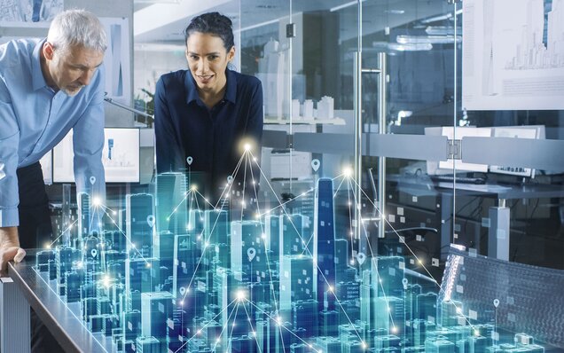 Das Bild zeigt eine virtuelle Großstadt und zwei Personen, die sich über digitale Vernetzungen austauschen. Die Vernutzung ist durch Linien und leuchtende Punkte auf den Gebäude gekennzeichnet.