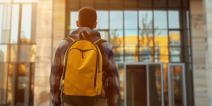 Schüler mit gelbem Rucksack vor Haupteingang einer Schule