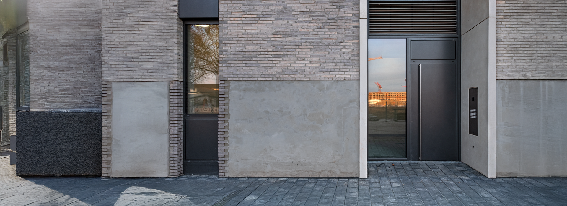 Fassade eines modernen Gebäudes mit Eingangsbereich, großem Fenster und markanten Baumaterialien