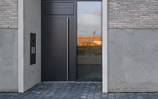 Moderner Hauseingang mit schwarzer Tür, Edelstahlgriff und Sprechanlage in urbanem Baustellenumfeld